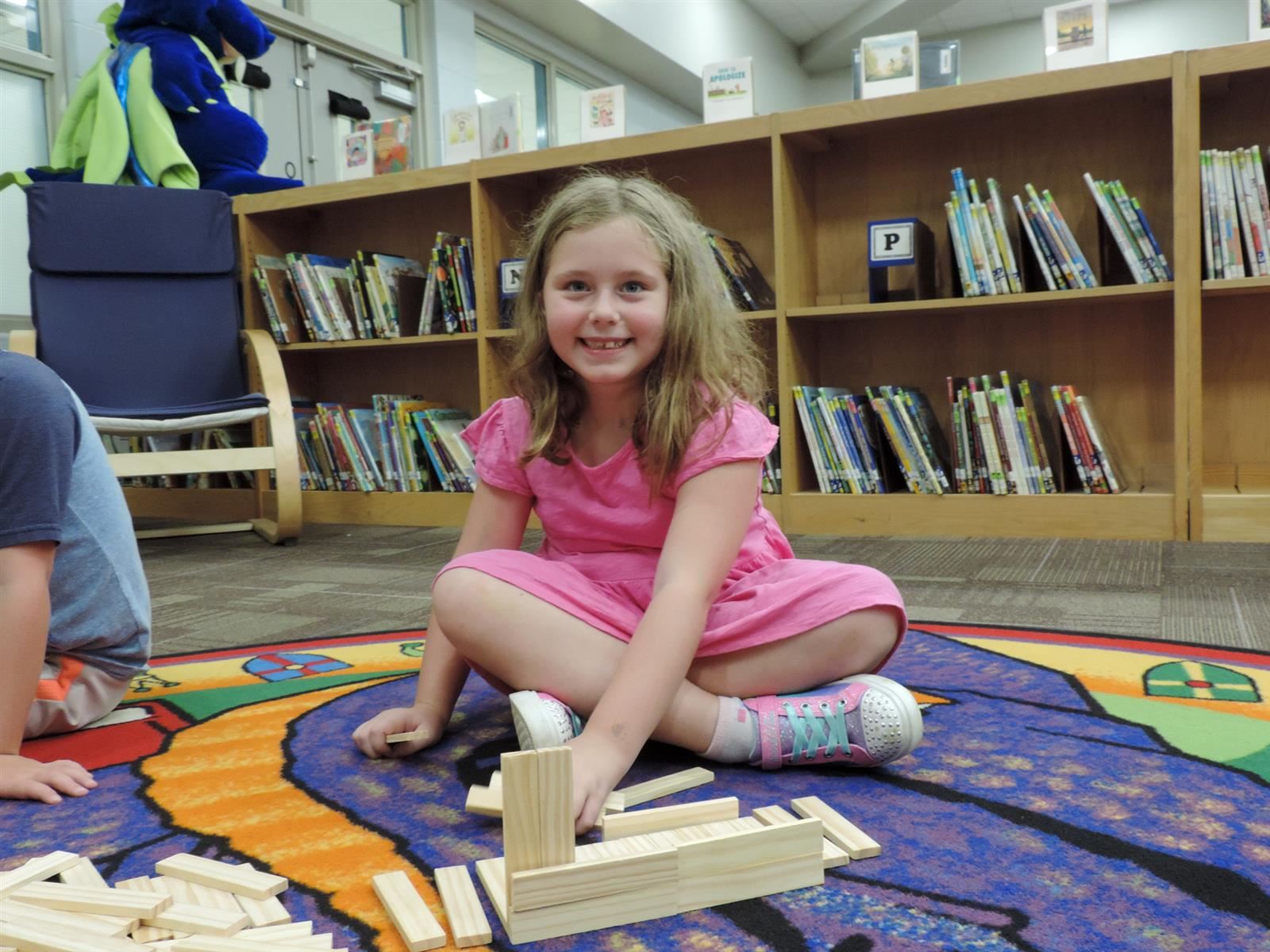 Girl in a pink dress building a wooden library